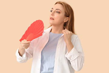 Canvas Print - Mature woman with fan suffering from hot flashes on beige background. Menopause concept