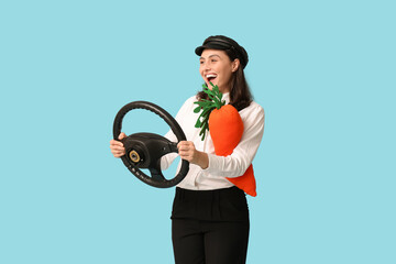 Wall Mural - Happy female taxi driver with toy carrot and steering wheel on blue background. Easter celebration