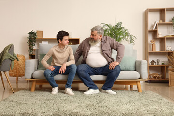 Sticker - Happy grandfather and his cute grandson sitting on sofa at home