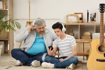 Sticker - Happy grandfather and his cute grandson with mobile phone in headphones listening music at home