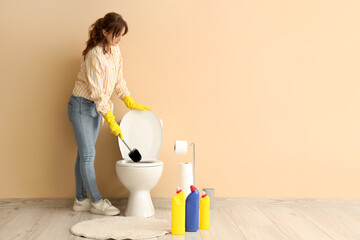 Canvas Print - Young woman cleaning toilet bowl with brush near beige wall