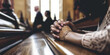A close-up of clasped hands on a church pew during a service, evoking a moment of prayer and reflection in a communal worship setting.