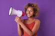 Young happy cute African American woman teenager with megaphone in hands smiling looking at camera and inviting friends from high school or college to fun party stands in purple studio.