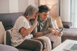 Video call concept. Happy senior retired woman sitting on sofa with young nephew waving hands video calling by mobile phone using technology for online webcam connection with distant family or friends