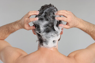 Canvas Print - Man washing his hair with shampoo on grey background, back view