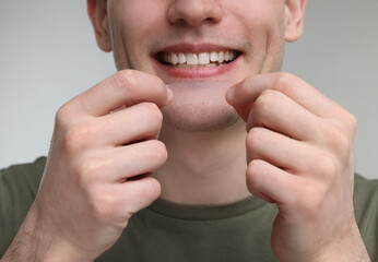 Wall Mural - Young man with whitening strip on light grey background, closeup