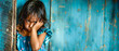 A little offended sad girl stands in front of a solid blue wall and looks directly. Child psychology. Relationship between parents and children. Banner. Copy space