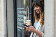 © Westend61 - Happy businesswoman holding disposable cup and using smart phone