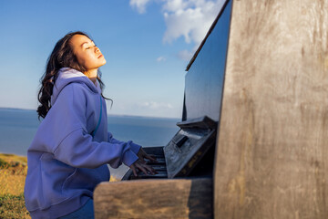 Wall Mural - An attractive Asian woman has closed her eyes and is playing the piano outdoors.