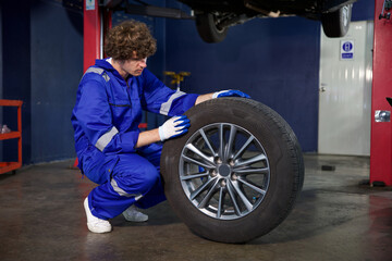 Wall Mural - mechanic holding and checking a tire for fixing in garage