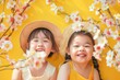 Cute and joyful Asian sisters against a sakura tree background. Happy children on yellow background