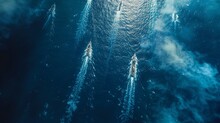 An Aerial View Of A Fleet Of Military Ships In Formation, Navigating Through Deep Blue Sea Waters Under A Clear Sky.