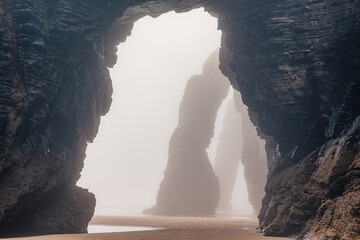 Wall Mural - Playa de Las Catedrales in foggy day. Catedrais beach in Ribadeo, Lugo, Galicia, Spain. Natural archs of Cathedrals beach. Moody rock formations on misty day. Travel destination