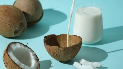 Wall Mural - Healthy vegan coconut milk pouring in coconut shell on blue background. Slow motion