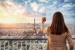 A tourist woman takes pictures with ther phone from the skyline of Paris, France, during sunset time