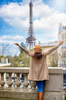 A happy woman with a french beret hat looks at the beautiful cityscape of Paris, France, with Eiffel Tower