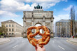Munich travel concept with a hand holding a traditiona,l german Bretzel in front of the Victory Gate, Germany