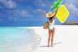 A happy woman in a white bathing suit walks down a tropical beach in the Maldives throwing a yellow floatie in the air