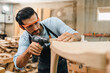© chokniti - Diligently skilled man work with wood in carpenter's shop, using tools and equipment to transform timber planks into bespoke wooden pieces, craftsmen workshop with natural material, furniture industry