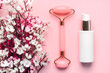 Closeup of jade massanger roller, facial cream bottle for skin care and almond blossoms. Skin care products concept