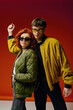 © LIGHTFIELD STUDIOS - appealing fashionable couple in stylish clothes with sunglasses posing on red backdrop together