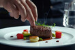 Close-up of a chef's hand arranging a steak dish on a white plate

