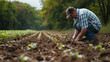 Farmer crouches in a field, carefully tending to his crops among long rows of fertile soil.