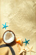 Straw hat, coconut, starfish and shells on white fine sand.