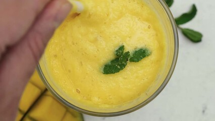 Wall Mural - Top view of man hand mixing yellow mango smoothie or milkshakewith a straw. Top view. Tropical healthy refreshment drink concept. Summer beverag