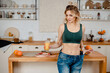 Pretty sporty woman with blond hair posing on camera in oversized jeans and holding glass with vitamin cocktail. Weight loss and diet concept.