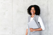 A poised African-American businesswoman stands confidently with her laptop, her smile exuding professionalism against a minimalist backdrop. This image captures the essence of modern corporate success