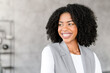 A radiant African-American businesswoman smiles confidently, standing in a modern office environment. Her professional attire and cheerful demeanor project both approachability and authority.