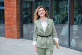 Fototapeta Desenie - Portrait of a successful business woman in front of modern business building. Young manager poses outside. Female business leader.
