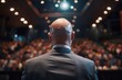 Rear view of a bald businessman addressing an attentive audience in a conference room. Concept of leadership and corporate events.