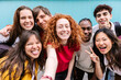 © Xavier Lorenzo - Diverse student friends group bonding together outdoors, taking selfie portrait standing over blue background. Youth community and teenage friendship concept.