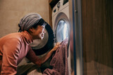Fototapeta Kwiaty - A happy japanese housewife is putting laundry into a washing machine in bathroom.