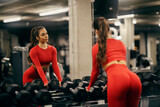 Fototapeta Kwiaty - Reflection in a mirror of fit sportswoman looking herself in a mirror in a gym.