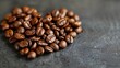   A mound of coffee beans on a gray table One area holds a heart-shaped indentation amidst the beans