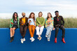 A group of diverse friends sitting on blue wall using cell phones online app