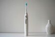 A modern electric toothbrush, standing upright on a white surface, with its bristles facing forward.
