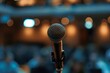 A professional microphone awaits the next speaker, with an out-of-focus audience in the backdrop, capturing the anticipation of a live event.