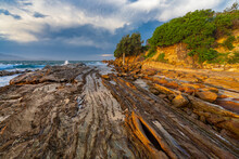Low Angled View Over A Rocky Coastline In Late Afternoon Light With A Dramatic Stormy Sky Overhead