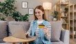  Happy young woman holding credit card and using laptop making payment online. Shopping, e-commerce, internet banking, spending money, working from home concept 