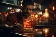 Un hombre con barba, Bartender o cantinero presentando un vaso con bebida y hielos en la barra de un bar. Al fondo la ambientacion del bar con luces suaves