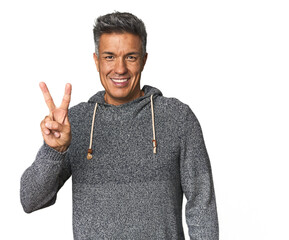 Middle-aged Latino man showing victory sign and smiling broadly.