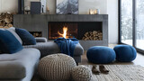 Fototapeta  - Grey sofa with blue pillows next to the fireplace and beige knit pouffes in between. a warm and inviting winter setting. Scandinavian interior design for a contemporary living room