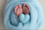 Fototapeta  - The tiny foot of a newborn baby. Soft feet of a new born in a blue wool blanket. Close up of toes, heels and feet of a newborn. Knitted blue heart in the legs of a baby. Macro photography. 