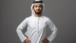 Confident young man in traditional Emirati attire posing with hands on hips. Smiling, studio shot on a grey background, cultural representation. AI