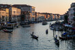 Scenic sunset view of Grand Canal (Grand Canale) with tourist gondolas in Venice, Veneto, Italy, Europe. Famous landmark cathedral San Simeon Piccolo. Gondoliers at golden hour. Urban summer tourism