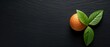   A tight shot of an orange and its attached leaf against a black surface, backed by darkness